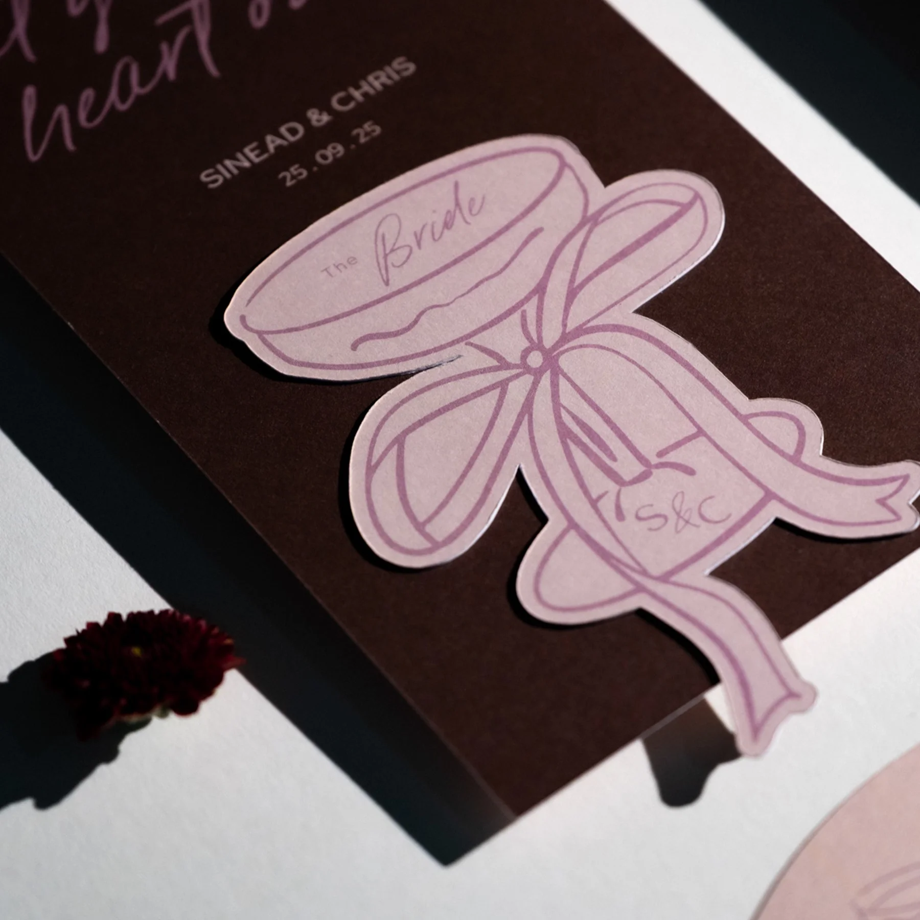 A wedding invitation featuring a pink sticker of a viola flower with handwritten text for the couple's names and wedding date.
