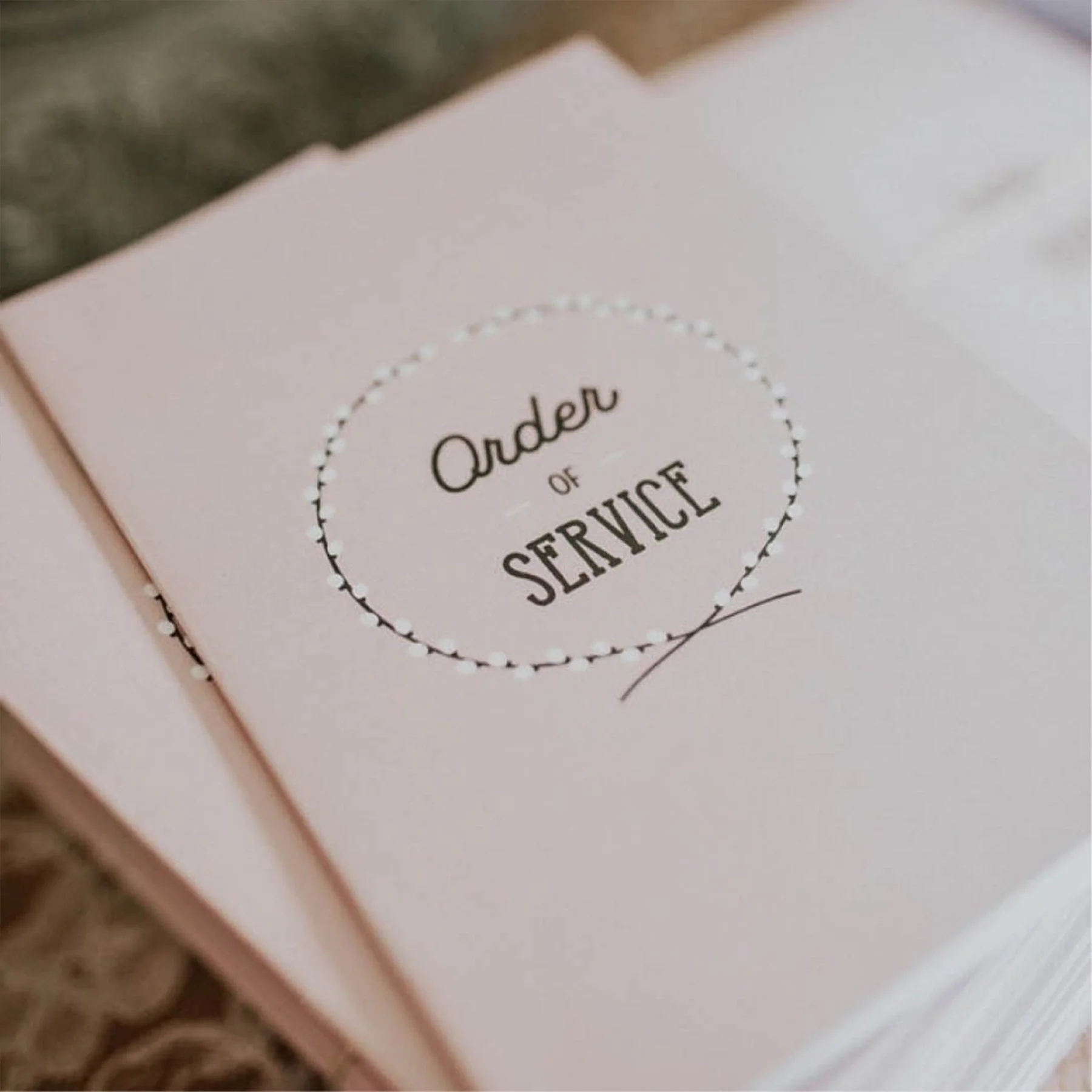 A pink booklet with the words "Order of Service" inside a dotted circle on the cover.