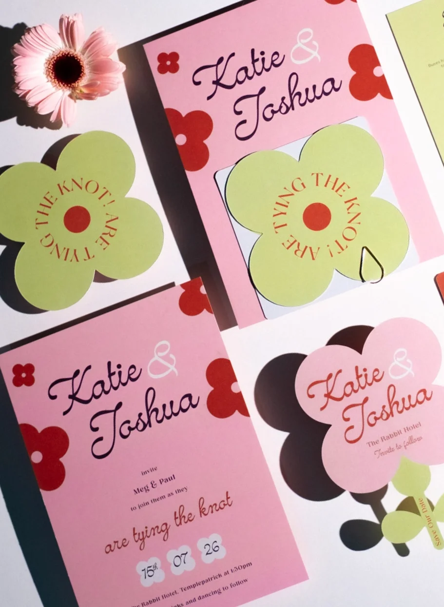 Wedding invitation cards for Katie and Joshua with floral designs in pink, red, and green, alongside a pink flower.