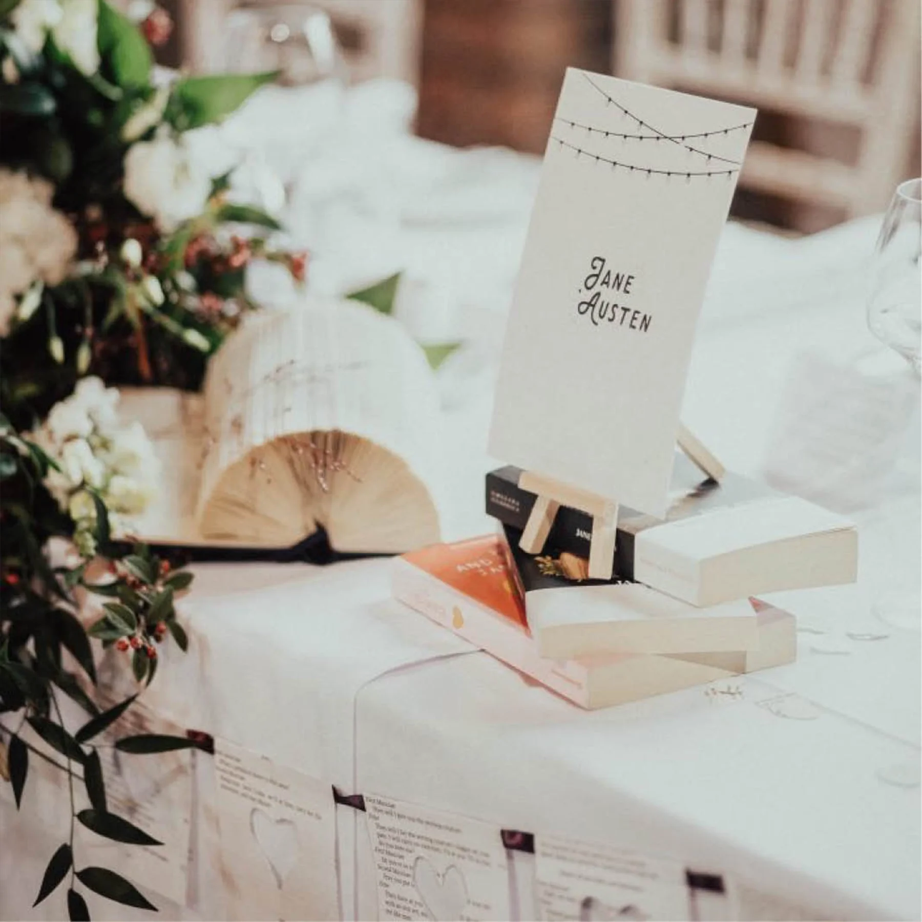 Table decorated with flowers, a table number card labeled 'Jane Austen', and small decorative books at a wedding reception.