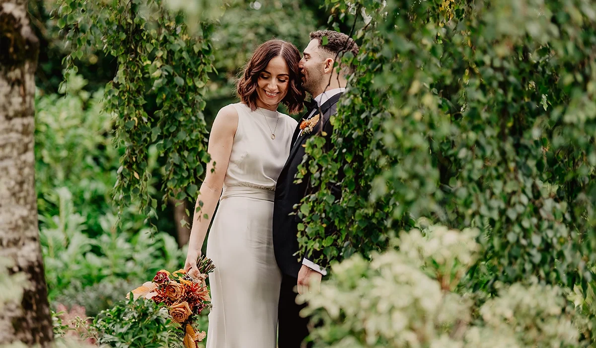 A bride and groom sharing a romantic moment in a lush garden, with the bride holding a bouquet of flowers.