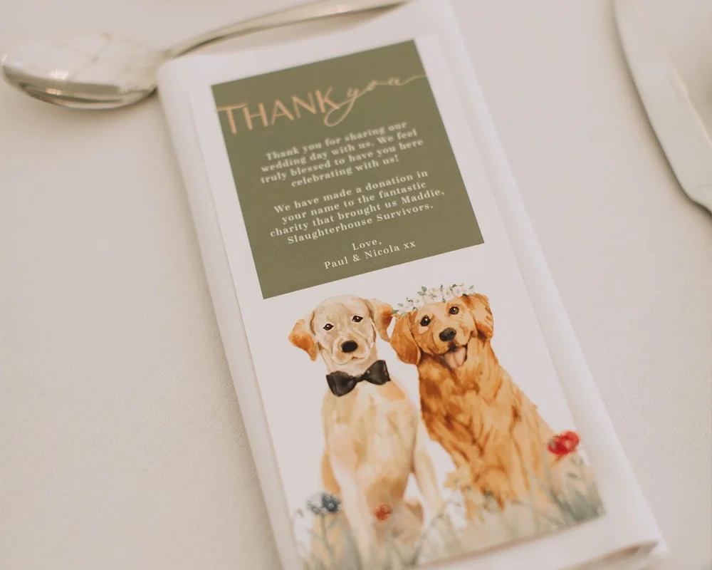 A thank you card with a painting of two dogs, one wearing a bow tie and the other with a flower crown, on a wedding table setting.