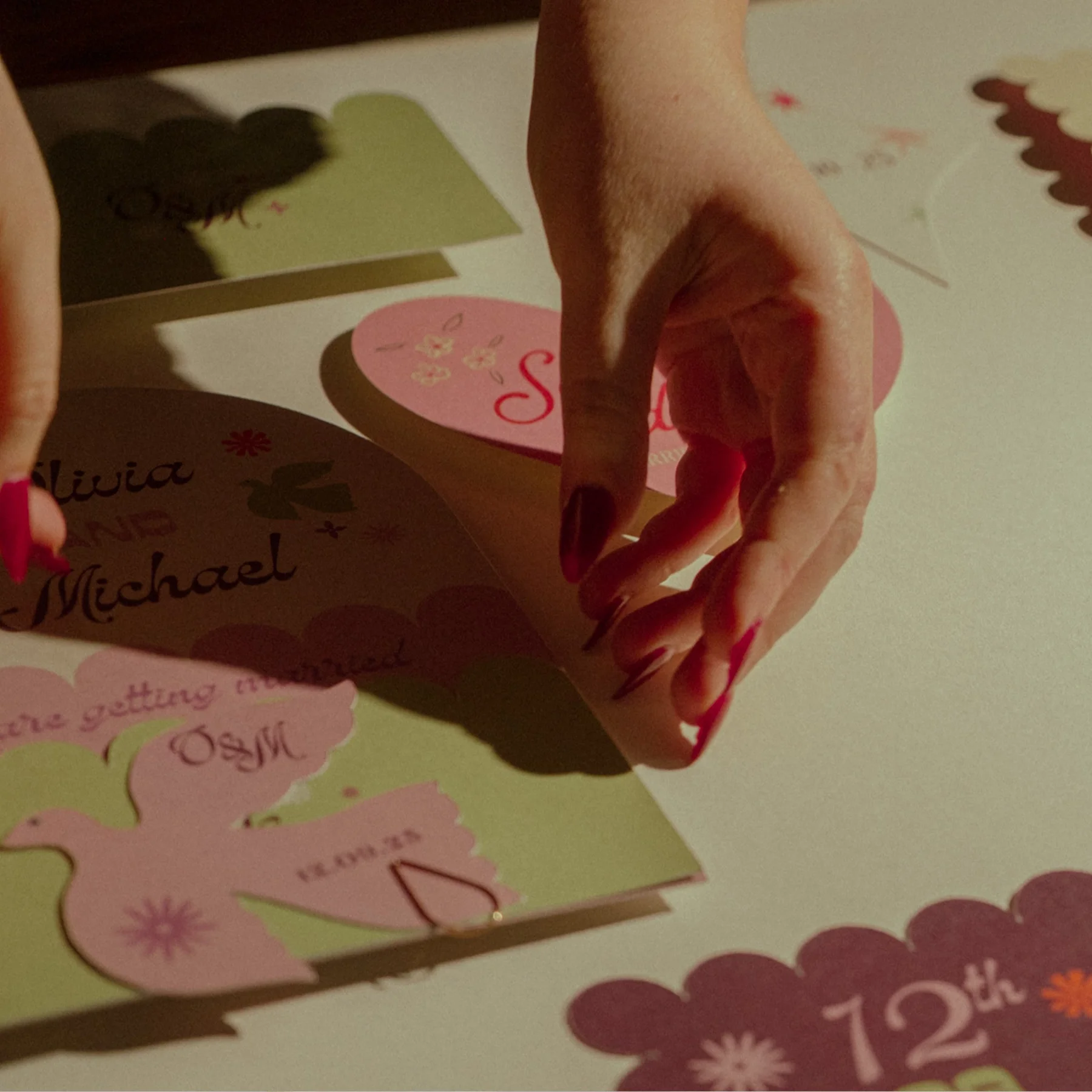 Person placing a pink heart-shaped card on a decorated surface with more pink and green heart and bunny cutouts with names and messages for a Valentine's Day celebration.