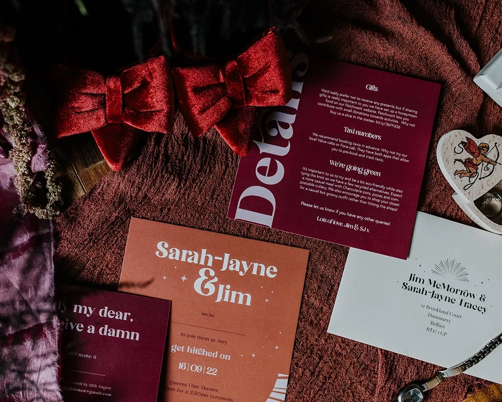 Collection of wedding invitation cards, a red velvet bow, and decorative items on a textured surface.