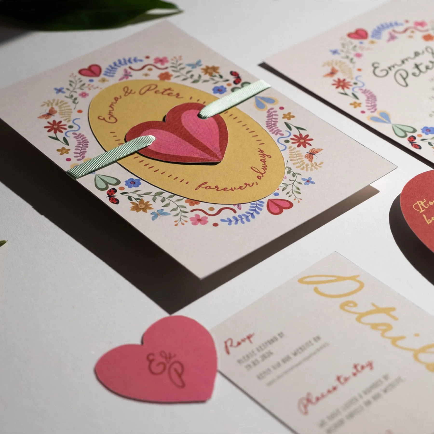Close-up of a wedding invitation with a pink heart and floral design, featuring the names Emma and Peter, and the phrase "forever, always".