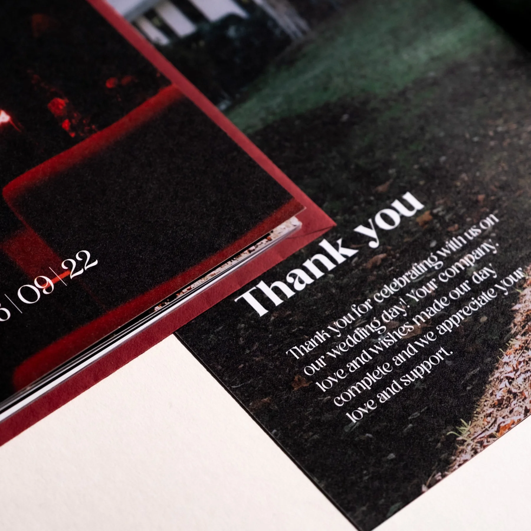 Close-up of wedding thank you card with white text on a black background, a blurred photo, and a small portion of a pink object.