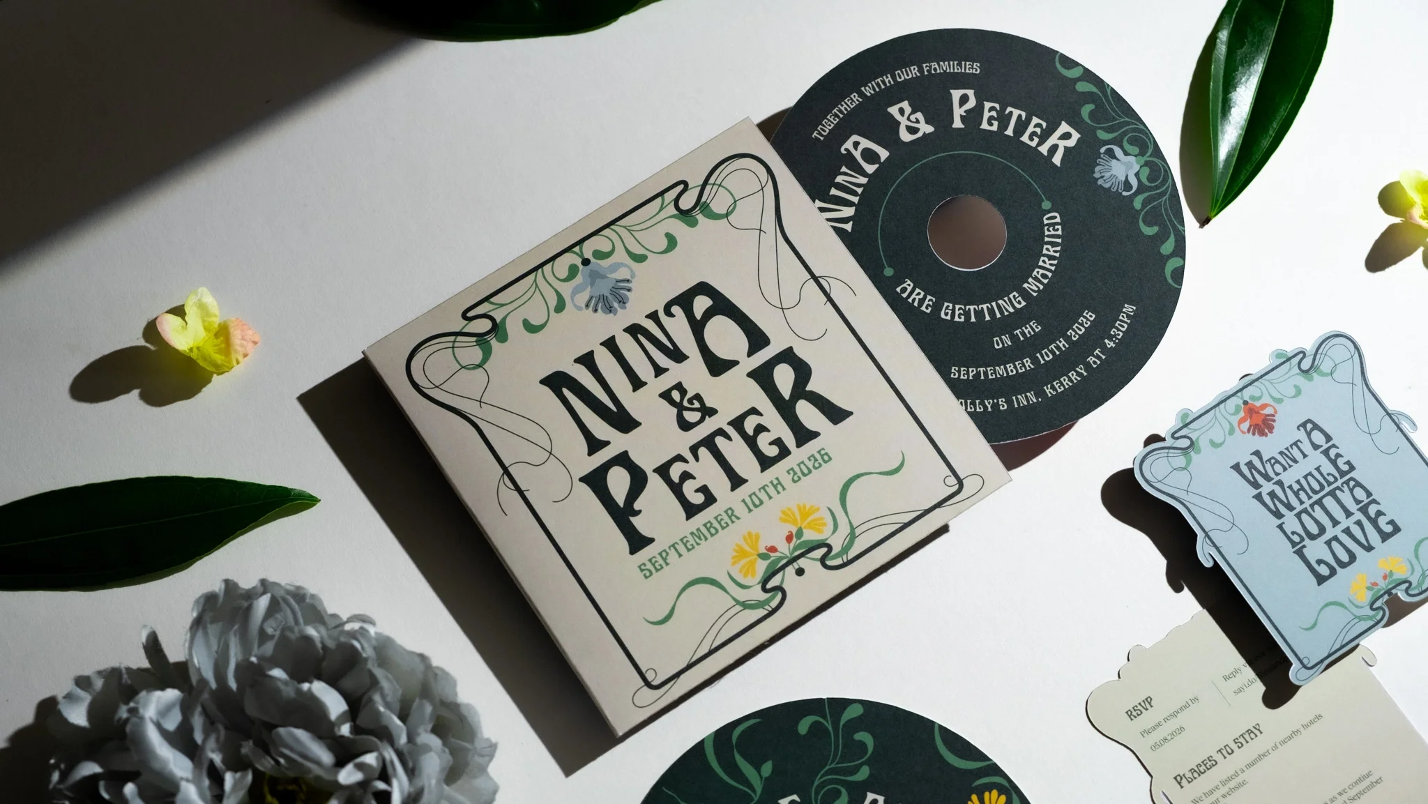 Wedding invitation suite with RSVP card, circle and rectangular tags, floral accents, and green leaves on white background, with small flower petals scattered around.