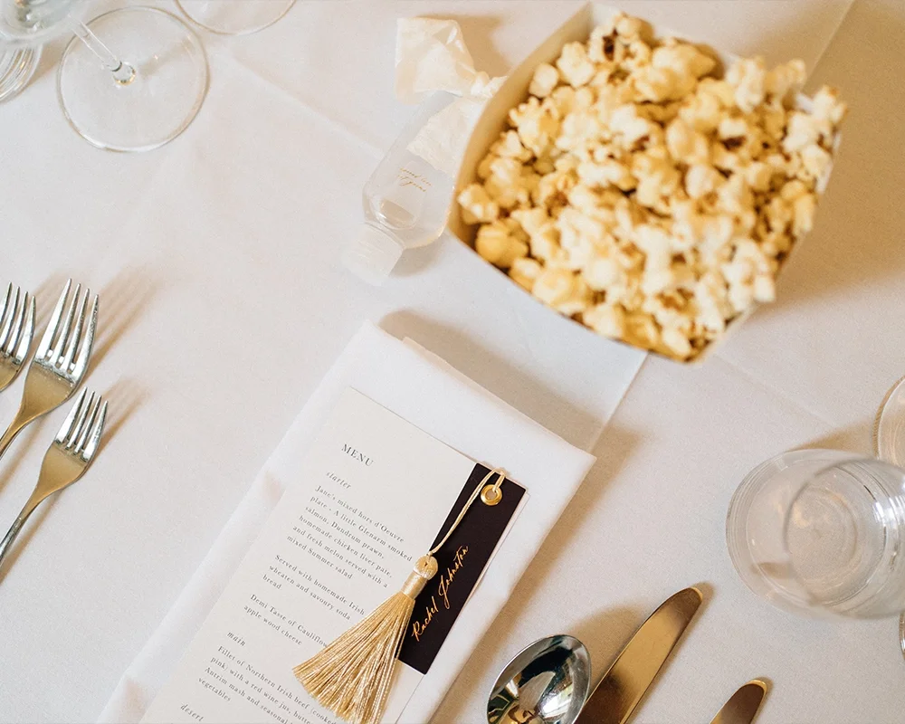 A table set with silver forks, a menu card with a gold tassel, and a large bowl of popcorn at a formal event.