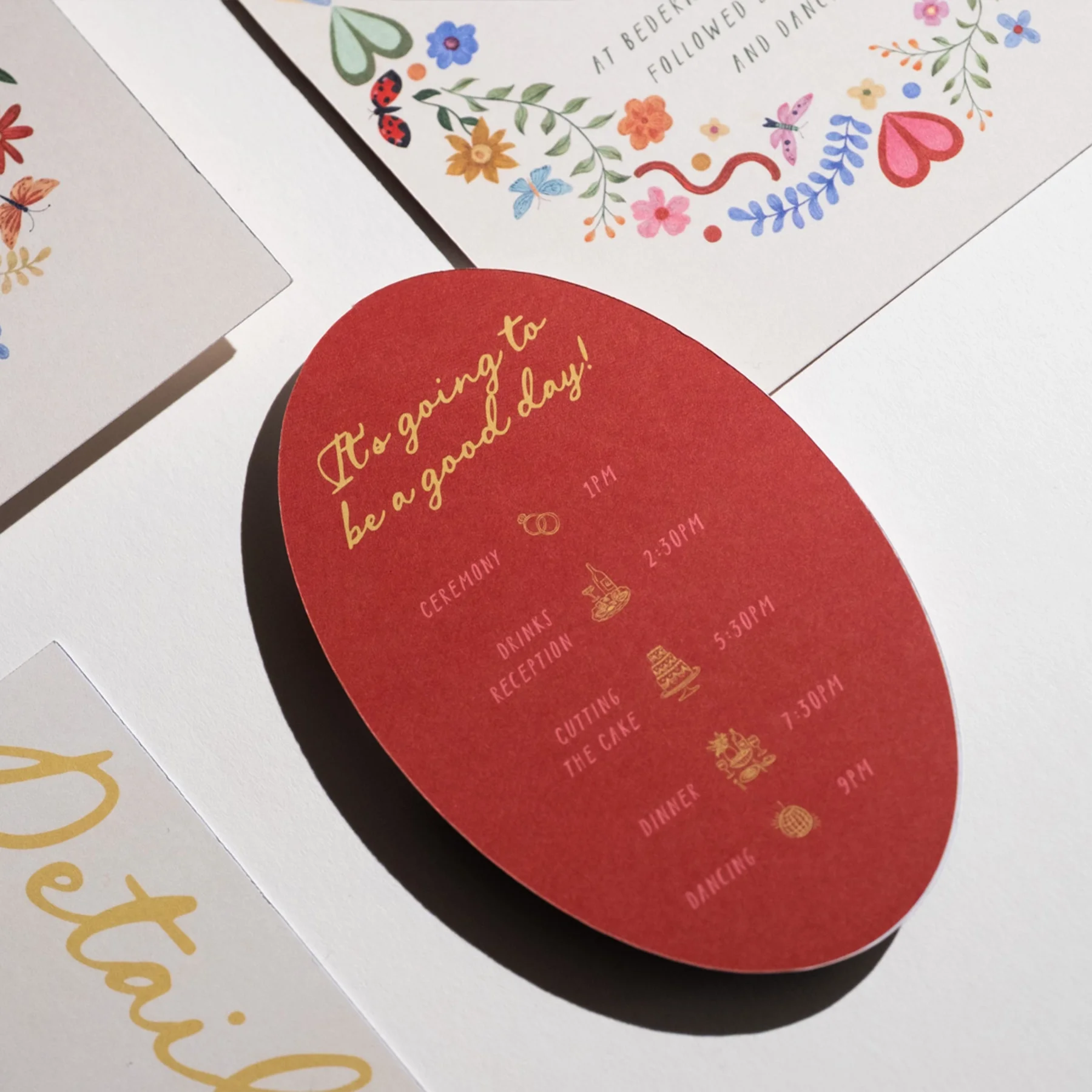 Invitation with a red background featuring gold cursive text that reads, 'It's going to be a good day!' and includes a detailed schedule of the wedding events with icons for ceremony, drinks reception, cutting the cake, dinner, and dancing.