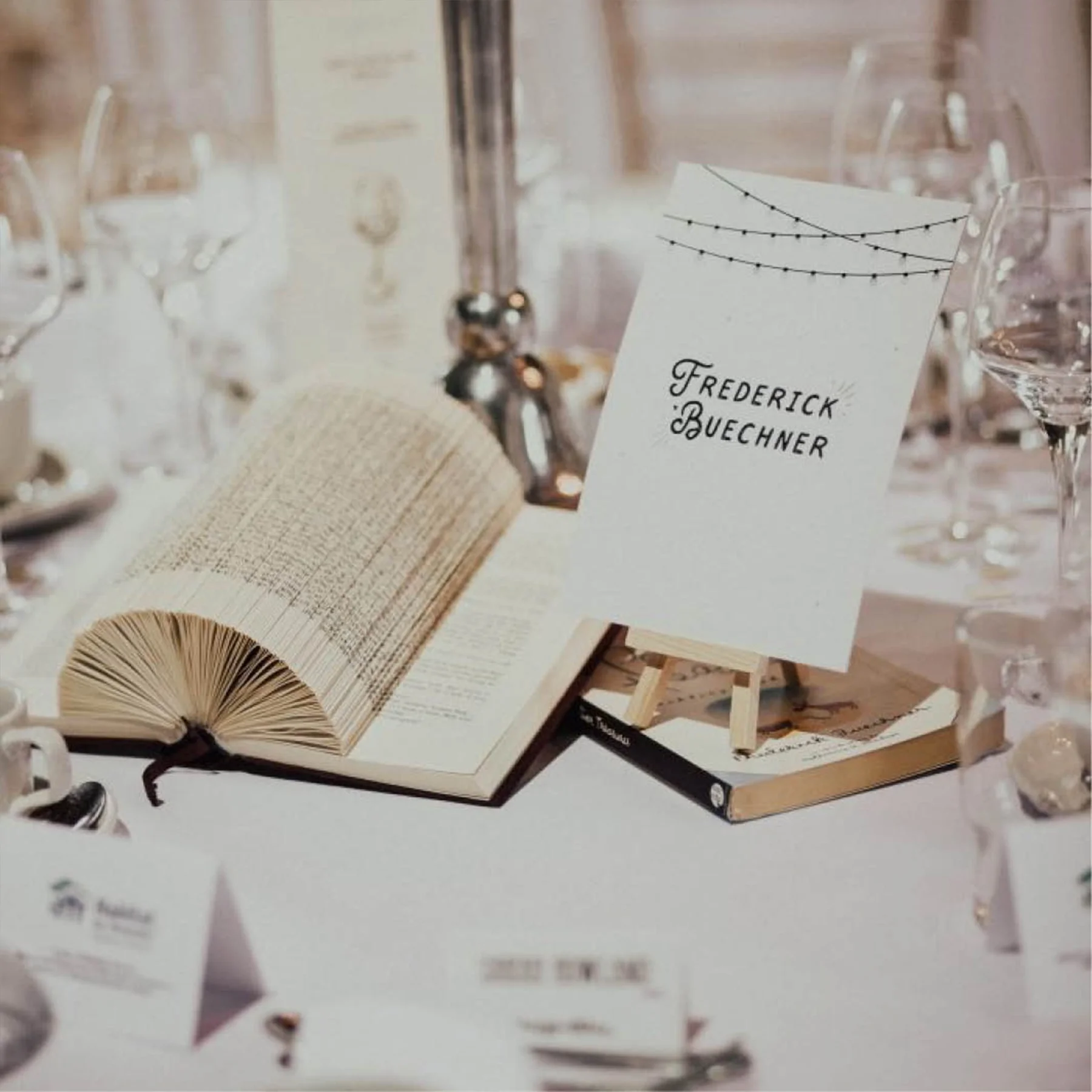 Table setting with an open book, a card with the name 'Frederick Buechner,' and glassware at an elegant event.