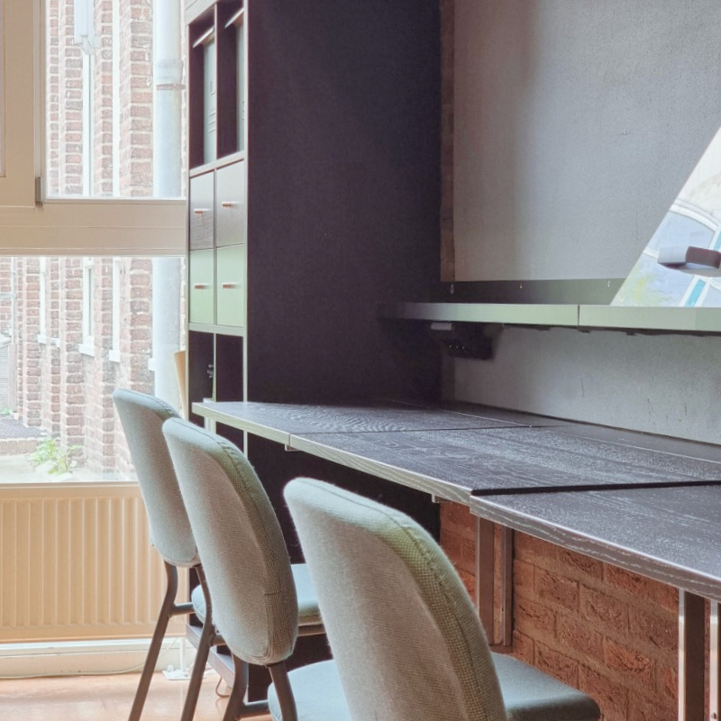 Moderne kantoorinrichting met flexibele werkplek aan een maatwerk blad, schilderijwandplanken, geïntegreerde stopcontacten en rustige zitplekken bij het raam voor efficiënt werken en overleg.