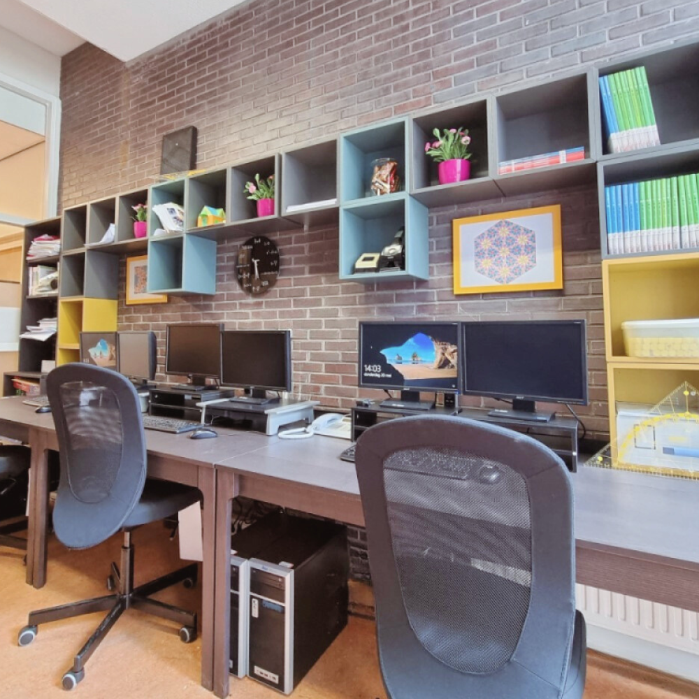 Industriële kantoorinrichting met drie werkplekken, maatwerk kastenwand, bakstenen muur en veel daglicht voor een efficiënte en overzichtelijke werkruimte.