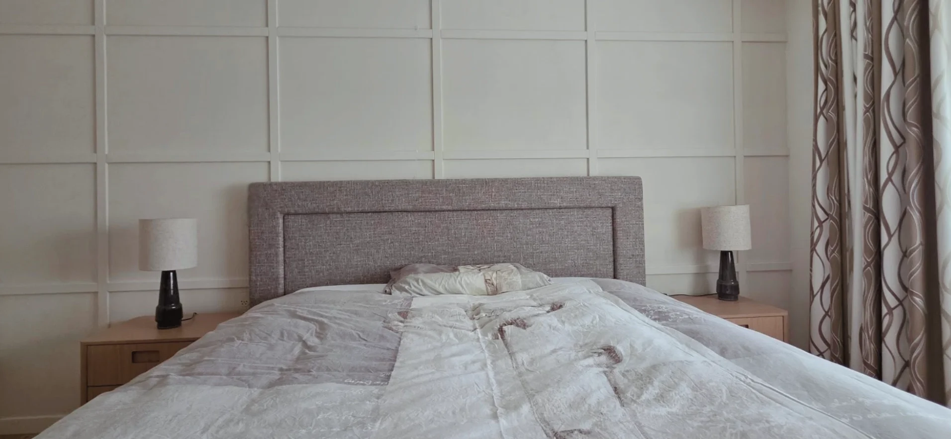 Frontaal beeld van de slaapkamer na restyling met paneelwand, gestoffeerd hoofdbord en neutraal beddengoed – interieuradvies, interieurontwerp en styling door En-Casa Interiors.