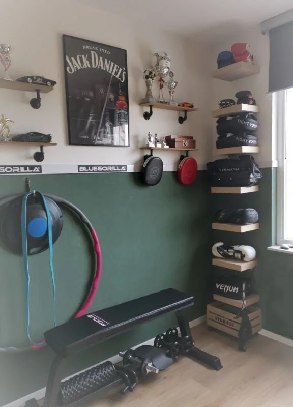 Deze sporthoek is stoer, praktisch en persoonlijk. En-Casa combineerde de groene lambrisering met industriële details en een strak opbergsysteem voor de sportitems. Zo krijgt de kamer karakter, maar blijft hij functioneel en zonder poespas.