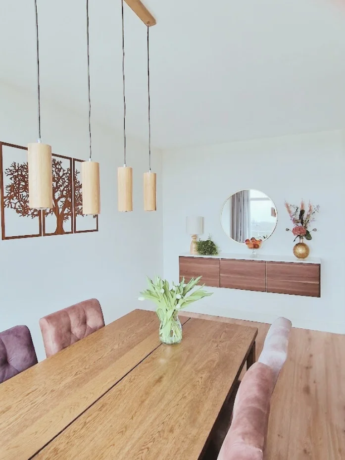 Eetkamerinspiratie met warme houttinten, zachte stoelen en rustige styling. Met wanddecoratie, spiegel en bloemen voor een sfeervol geheel.  Interieuradvies, interieurontwerp en styling door En-Casa Interiors in Noord-Holland.