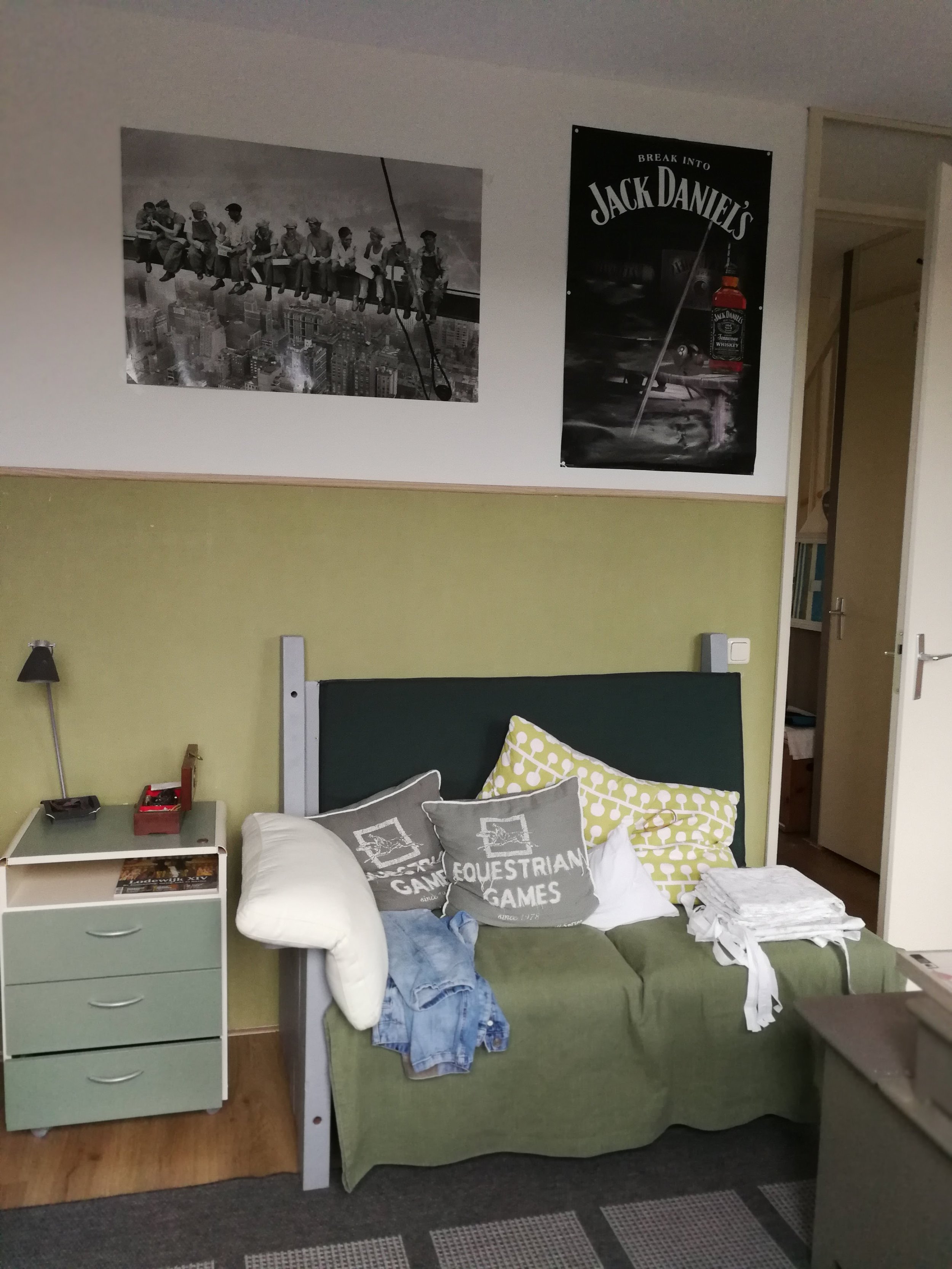Voor-situatie van de slaapkamer: een praktische kamer, maar met een wat onrustige uitstraling door de combinatie van kleuren, losse accessoires en verschillende stijlen. Het bed staat tegen de wand met een groene basis, aangevuld met meerdere kussens