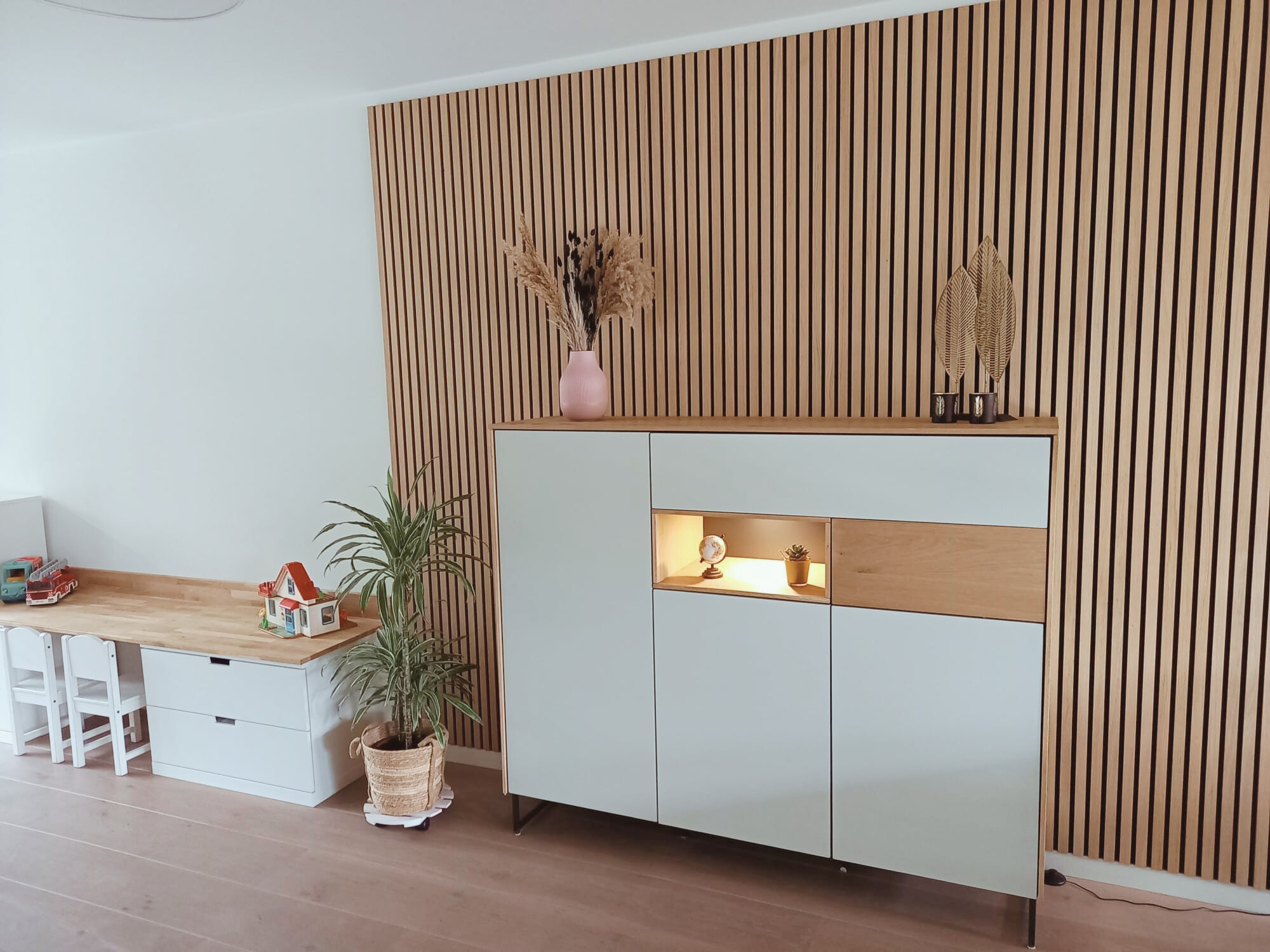 Stijlvolle wand met houten lattenpaneel en strak dressoir in zachte groentint, met warm verlichte nis voor decoratie. Een moderne, rustige basis met natuurlijke materialen en een speels detail — voor een en casa dat klopt in sfeer en functionaliteit.