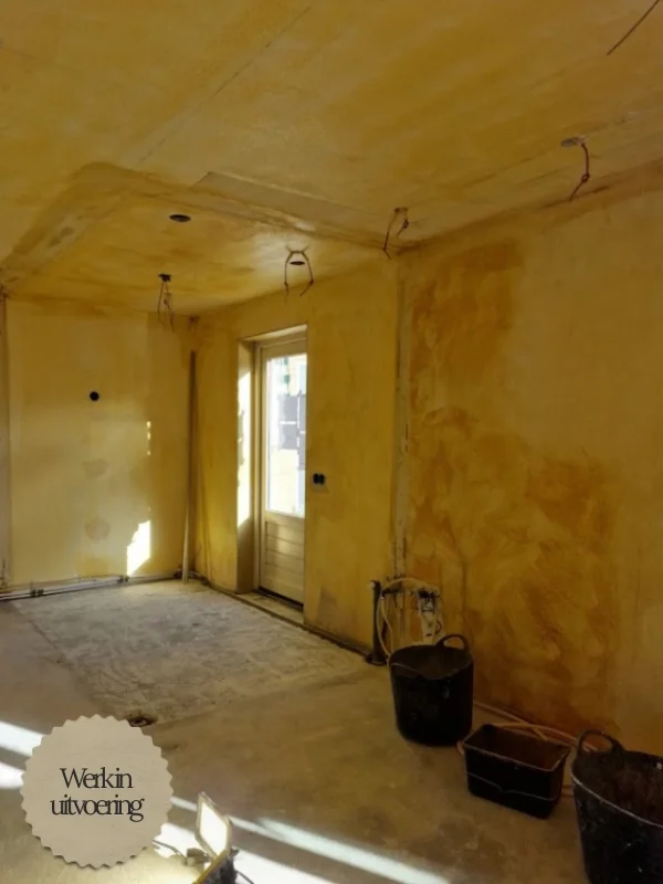 Ruimte tijdens verbouwing met kale betonnen vloer, onafgewerkte wanden en plafond.