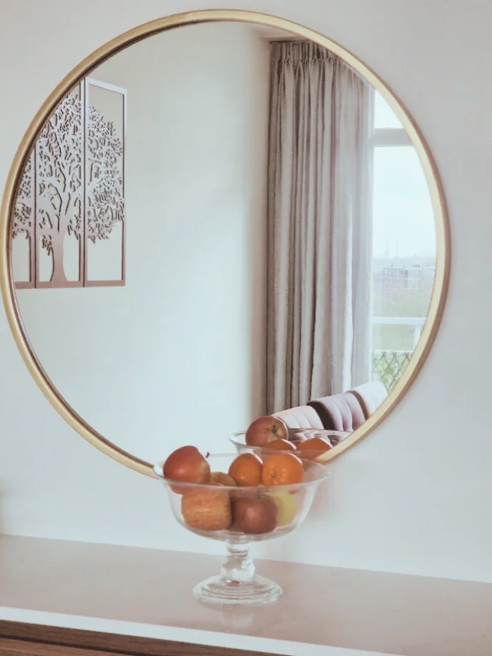 Interieurdetail: ronde spiegel als eyecatcher met subtiele goudtint en een fruitschaal op het dressoir. Minimalistisch, warm en in balans.  Interieuradvies, interieurontwerp en styling door En-Casa Interiors in Noord-Holland.
