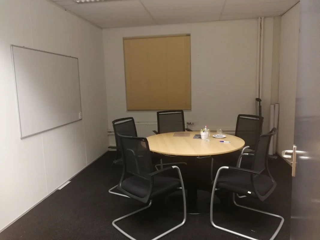 Vergaderruimte vóór herinrichting en interieurontwerp. Ronde vergadertafel, vergaderstoelen en whiteboard in een functionele kantoorruimte.