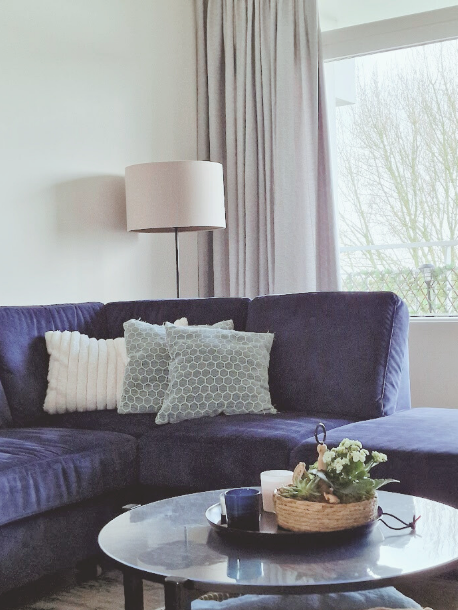 Close-up van een gezellige zithoek met donkerblauwe bank, zachte kussens en ronde salontafel. Neutrale tinten en lichtinval geven rust.