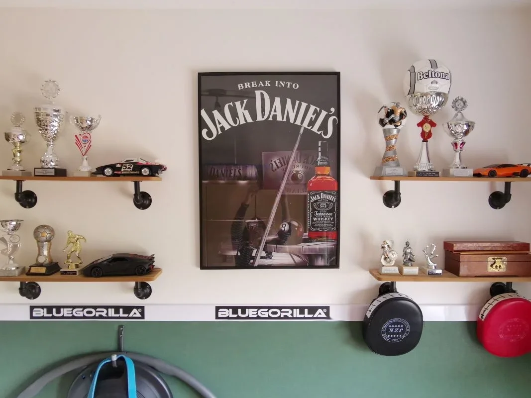 Deze wand maakt de kamer echt eigen. En-Casa bundelde alle herinneringen van de jonge man op industriële planken, strak geordend en mooi in beeld. Zo blijft de ruimte rustig, maar krijgt hij wel een persoonlijk verhaal.