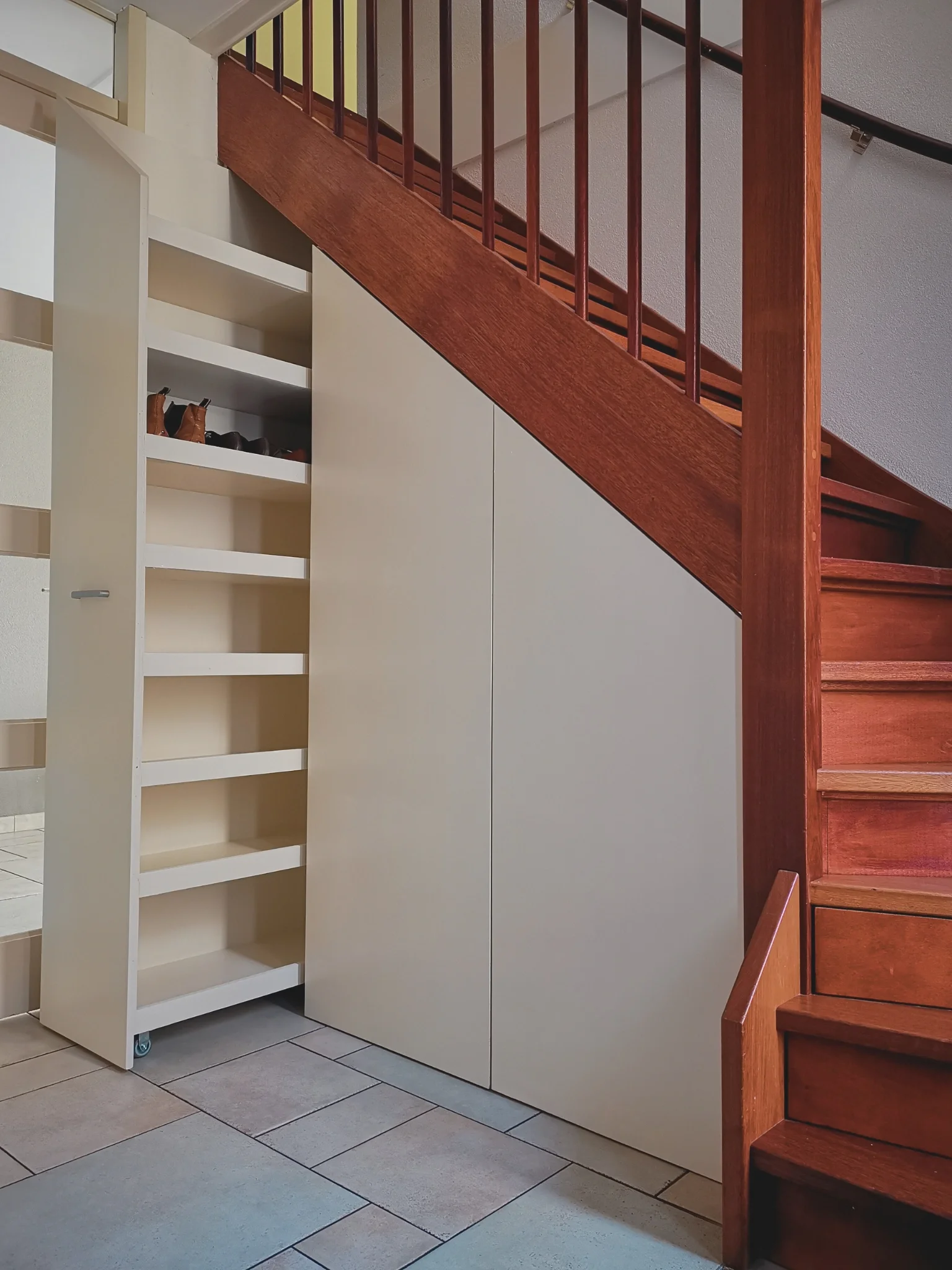 Maatwerk trapkast met uittrekbare opbergruimte voor schoenen en accessoires in de hal, ontworpen door En-Casa Interieuradvies in Heemskerk, Noord-Holland.