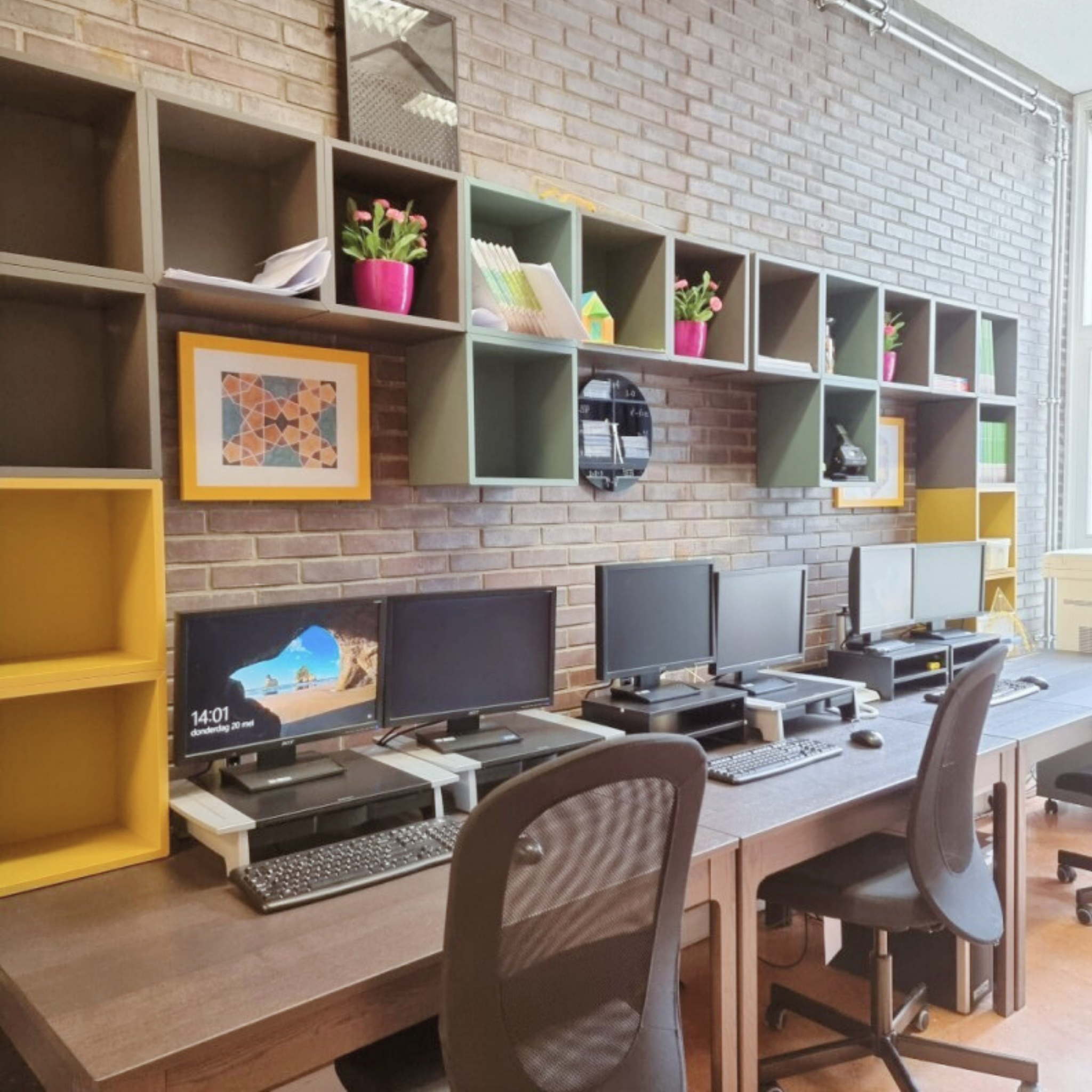 Moderne industriële kantoorinrichting met lange werktafel, meerdere werkplekken, maatwerk kastenwand en veel daglicht voor een efficiënte werkruimte.