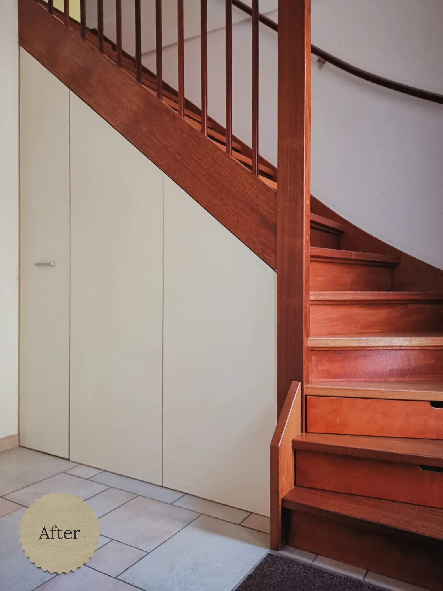 Op maat gemaakte trapkast met strakke, lichte kastdeuren naast een warme houten trap in de entree.