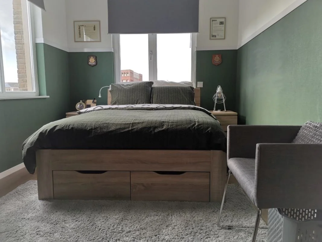 In de slaapruimte creëerde En-Casa een rustige, volwassen basis met groene lambrisering van behang en een witte bovenzijde. Zo blijft de kamer licht en luchtig, maar krijgt hij wel karakter. Het bed met opberglades zorgt voor extra praktisch gemak, z