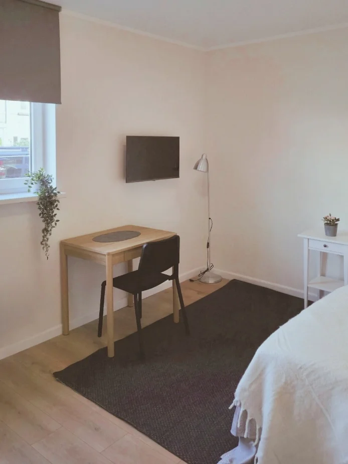 Een compacte, functionele slaapkamerhoek met werkplek: een houten bureau met stoel, tv aan de wand en zachte neutrale kleuren — praktisch ingericht voor werken, ontspannen en slapen in één rustige ruimte.