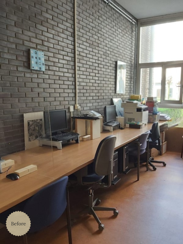 Before situatie van de kantoorinrichting met eenvoudige werkplekken langs een bakstenen muur, losse bureaus en beperkte opbergruimte, met daglicht vanuit het raam aan het einde van de ruimte.