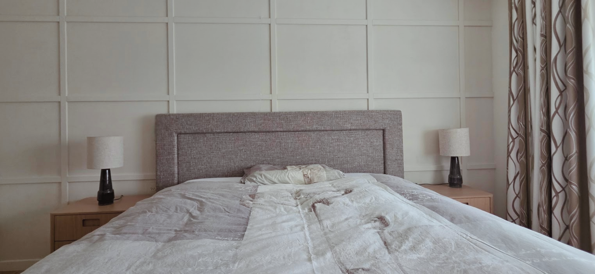 Frontaal beeld van de slaapkamer na restyling met paneelwand, gestoffeerd hoofdbord en neutraal beddengoed – En-Casa interieuradvies.