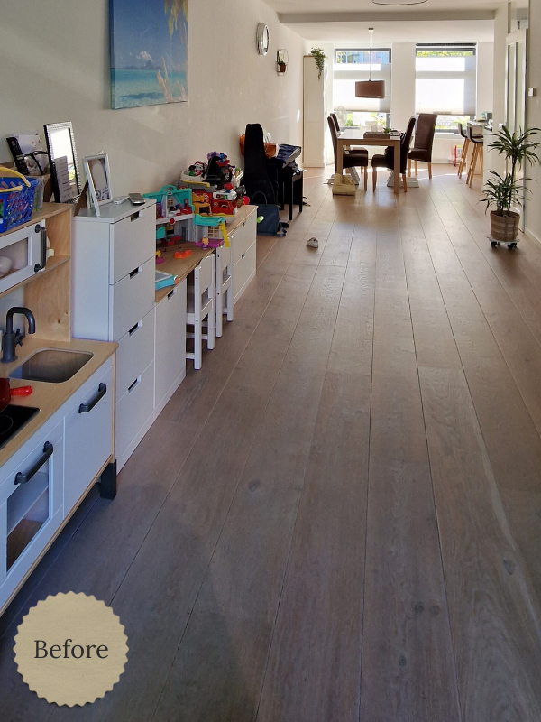 Voorfoto van een lange, lichte woonkeuken met witte keukenopstelling en warme houtlook vloer, met zicht richting de eethoek.