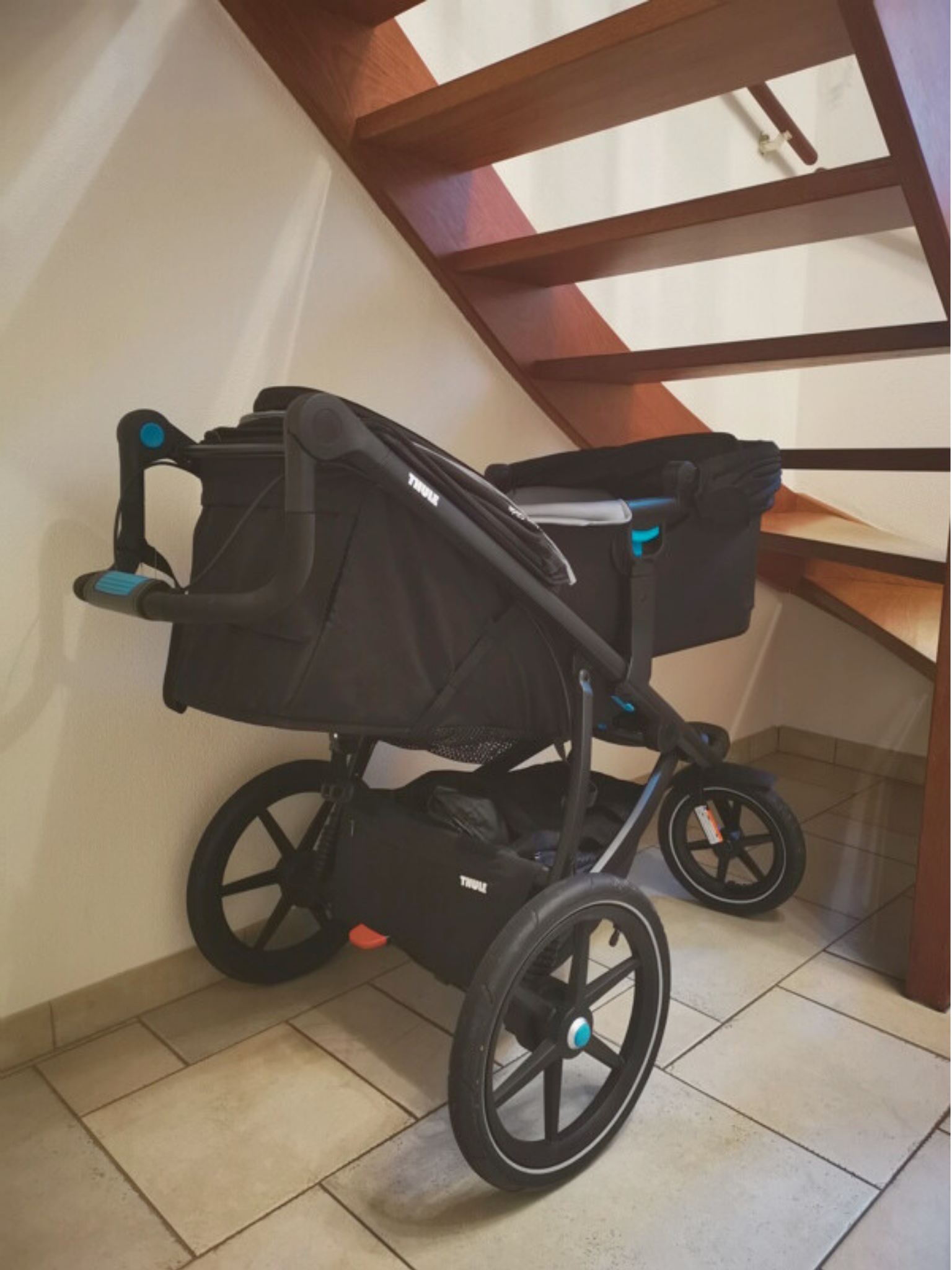 Kinderwagen onder een houten trap in de entree zonder goede opbergruimte.