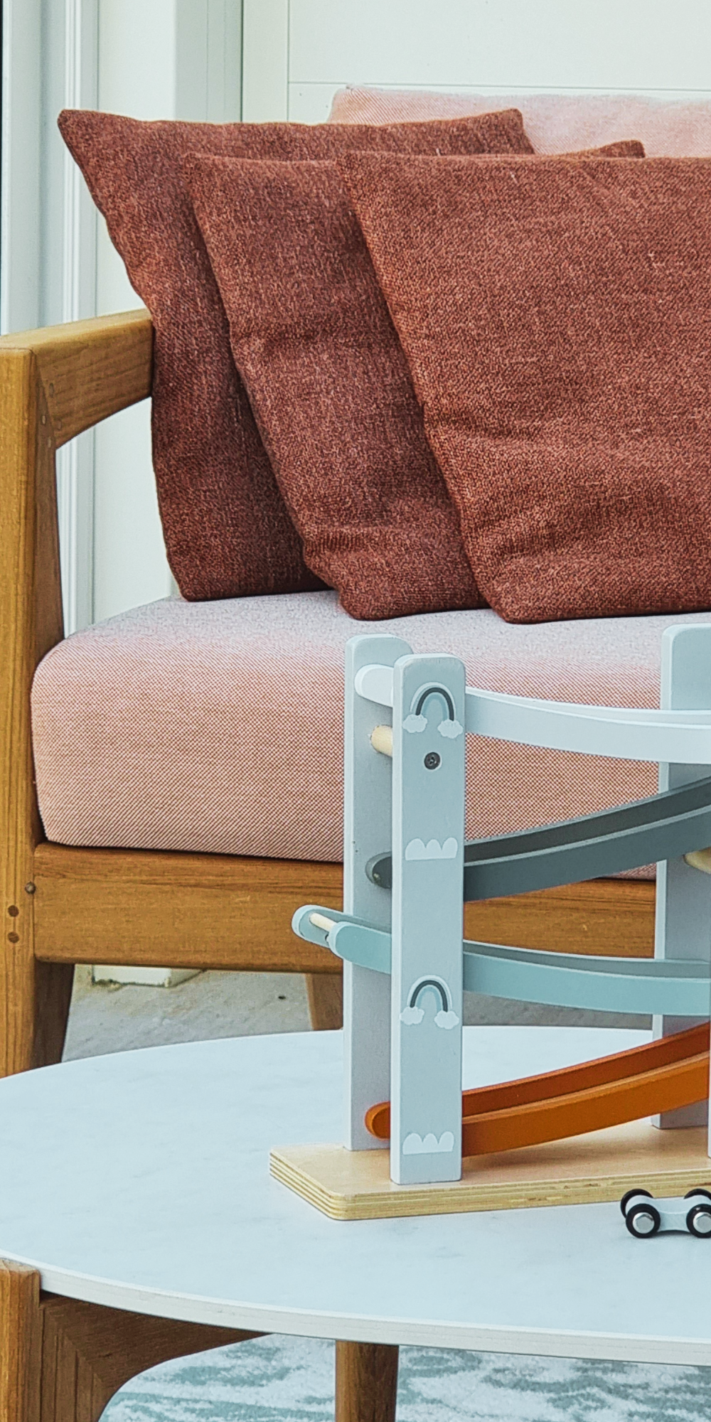 Detail van houten loungebank met terracotta kussens en zachte roze zitting, met kindvriendelijk speelhoekje.