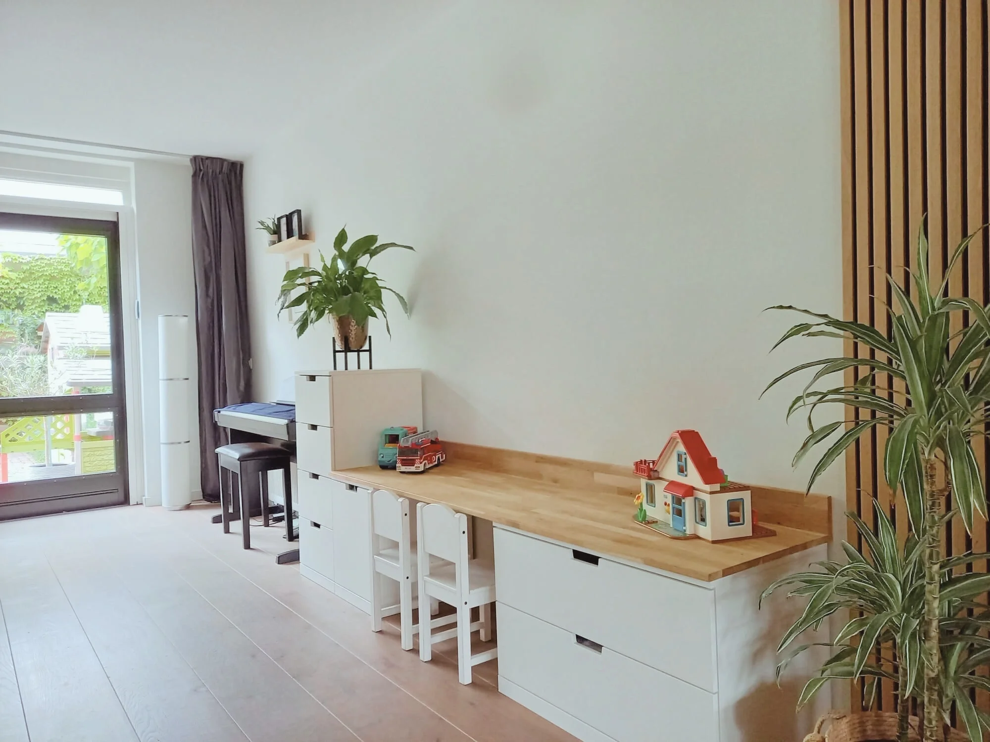 Lichte, multifunctionele hoek met lang houten werkblad op witte kasten, planten en een speels kinderhoekje. Neutrale basis met natuurlijke materialen en veel daglicht — praktisch, rustig en gezellig en casa.  Interieuradvies, interieurontwerp en styl