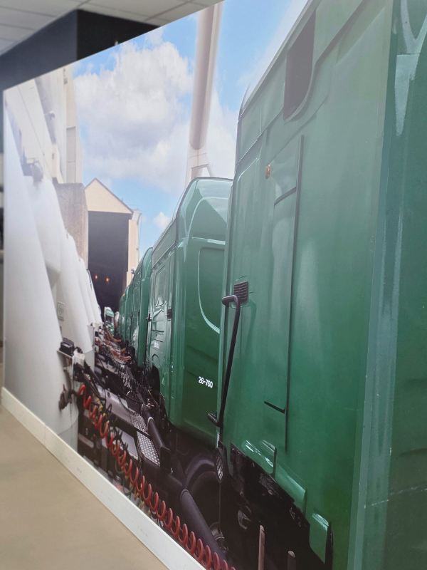 Detail van de wand tussen de kantine en de spoelbak met een fotoprint van de nieuwe vrachtauto’s voor het vervoer van cement. De krachtige groene trucks en het industriële beeld zorgen voor een stoer accent en versterken de identiteit van de locatie.