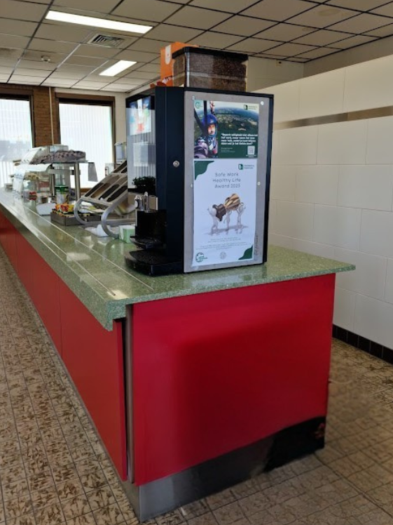 Before-situatie van de kantine: rode uitgiftebalie met groene counter en tegelvloer, een gedateerde maar functionele basis als startpunt voor de herinrichting en modernisering van de lunchruimte.