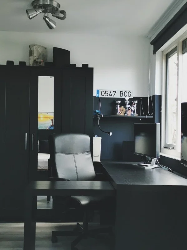 Moderne jongensslaapkamer met zwart bureau, ergonomische bureaustoel en strakke wandkast, ingericht als stijlvolle werkplek