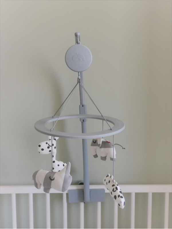 Close-up van een baby mobiel boven een wit ledikant. De mobiel is uitgevoerd in zachte grijs- en wittinten en heeft hangende figuurtjes, waaronder een olifantje en dieren met stippen. Tegen de rustige, zachtgroene muur zorgt dit detail voor een lieve