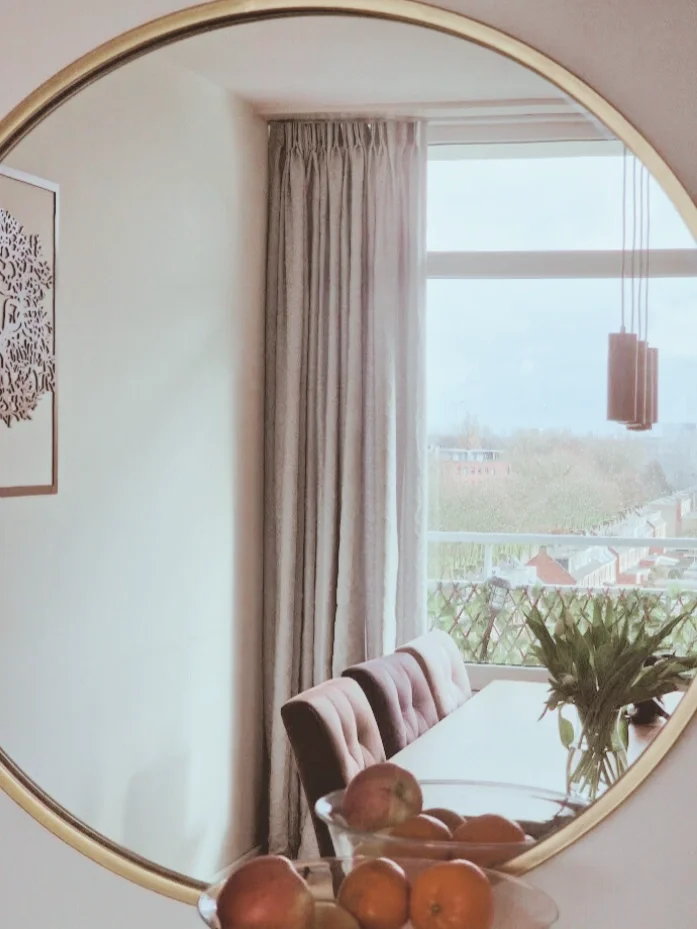 Interieurdetail: ronde spiegel met doorkijk naar de eethoek. Neutrale tinten, hout en textiel geven de ruimte een fijn en casa gevoel.  Interieuradvies, interieurontwerp en styling door En-Casa Interiors in Noord-Holland.