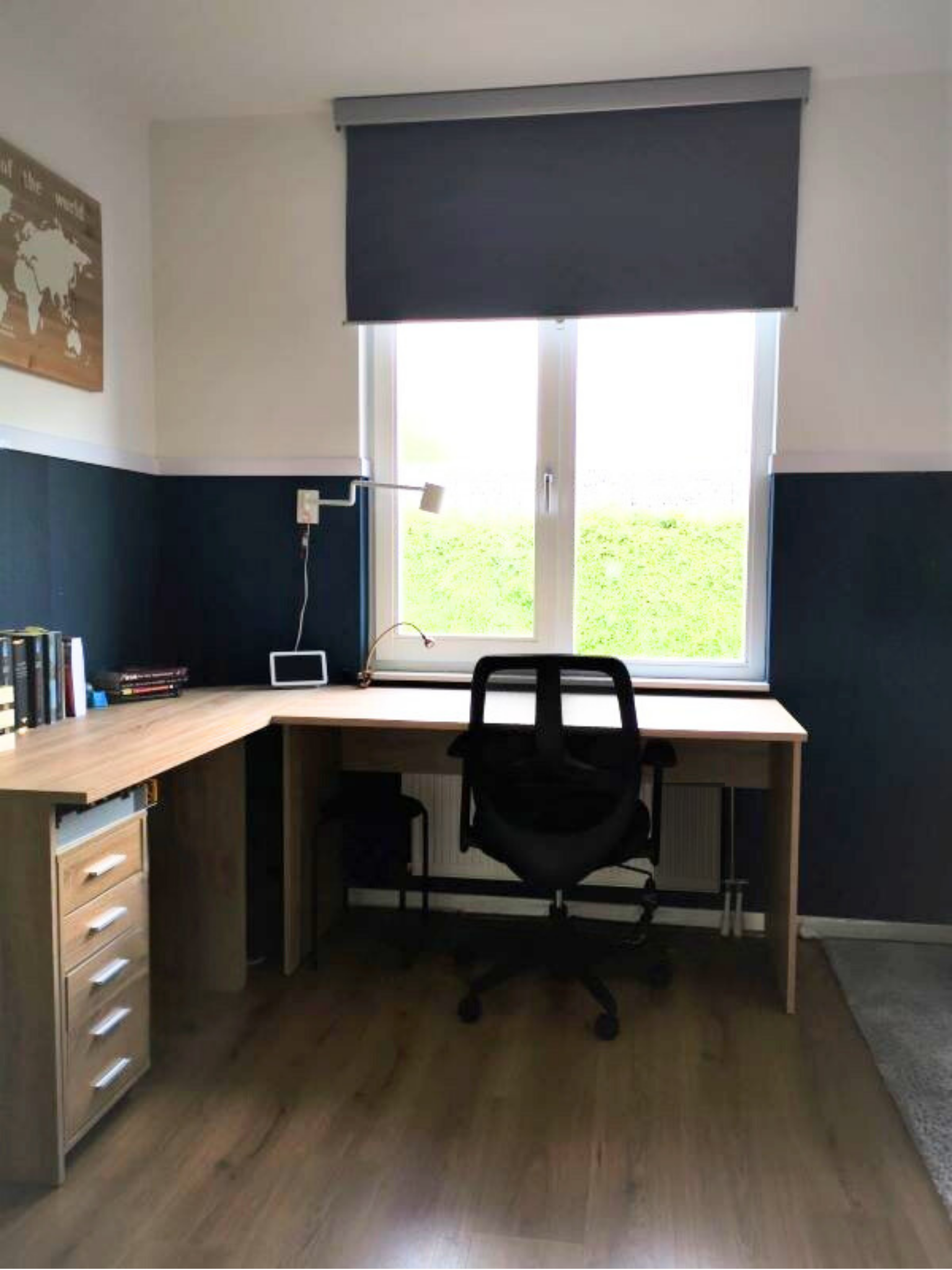 en praktische en rustige werkplek met veel daglicht. Het hoekbureau benut de ruimte slim en biedt genoeg werkoppervlak, terwijl de donkere (blauwgrijze) tint op de wanden zorgt voor een kalme, geconcentreerde sfeer. Door de eenvoudige inrichting en d