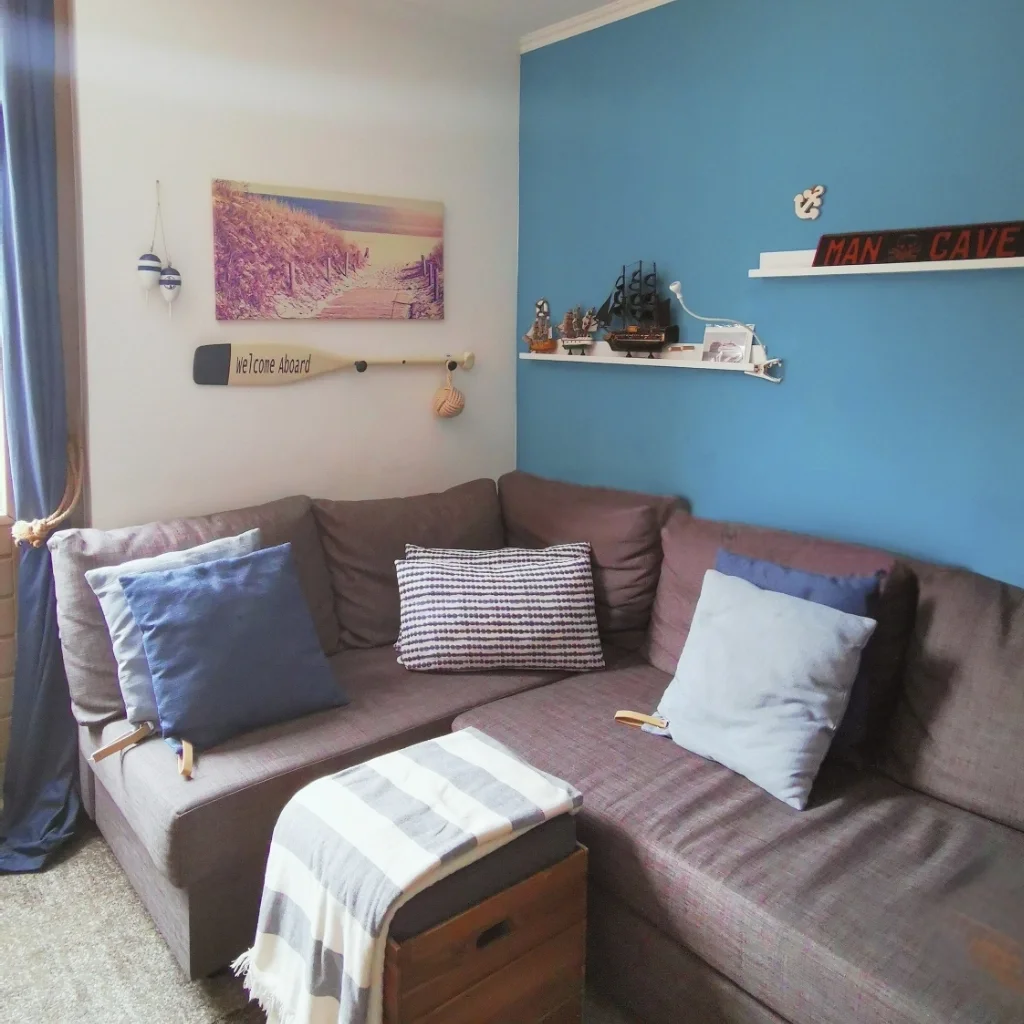 Knusse man-cave zithoek met blauwe accentwand, comfortabele bank en warme styling – onderdeel van een multifunctionele garage make-over met interieuradvies en styling door En-Casa Interiors in Heemskerk.