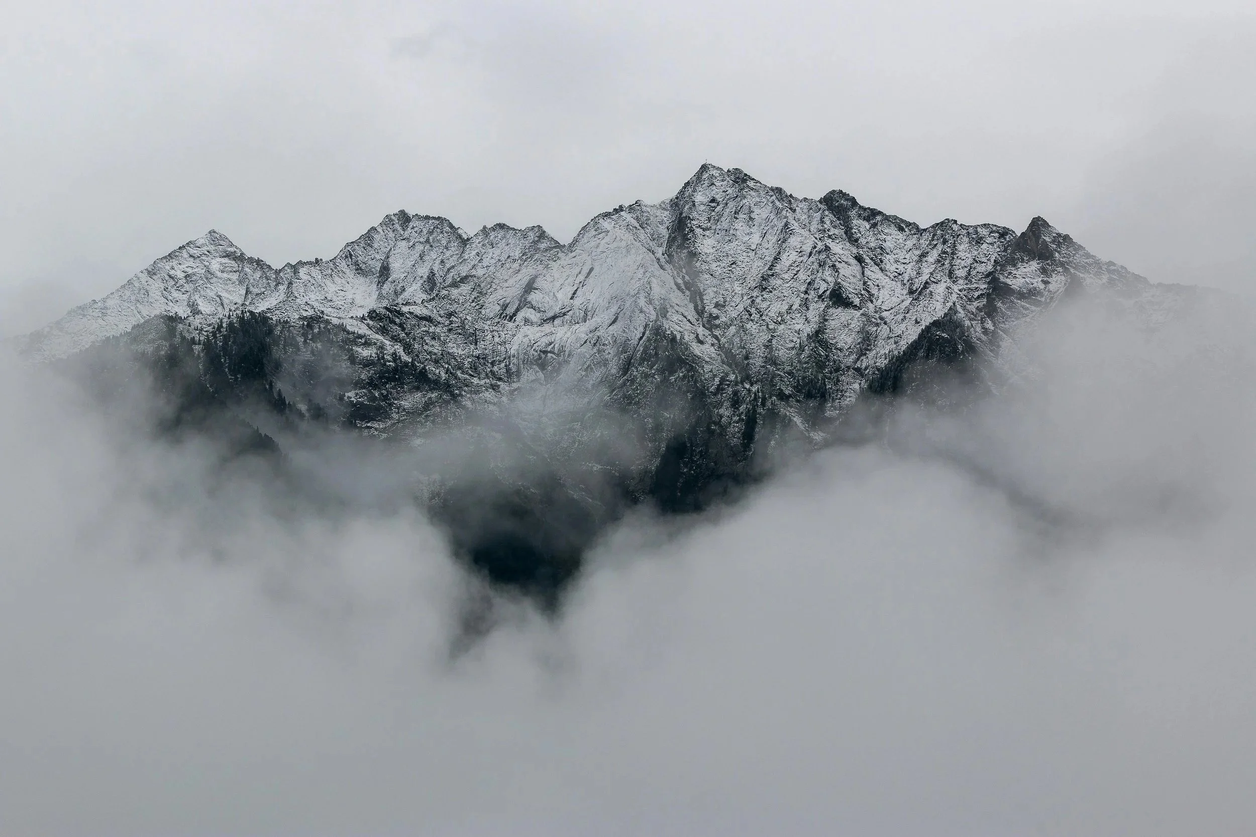 Snow-capped mountain peaks emerging above clouds and mist on an overcast day.
