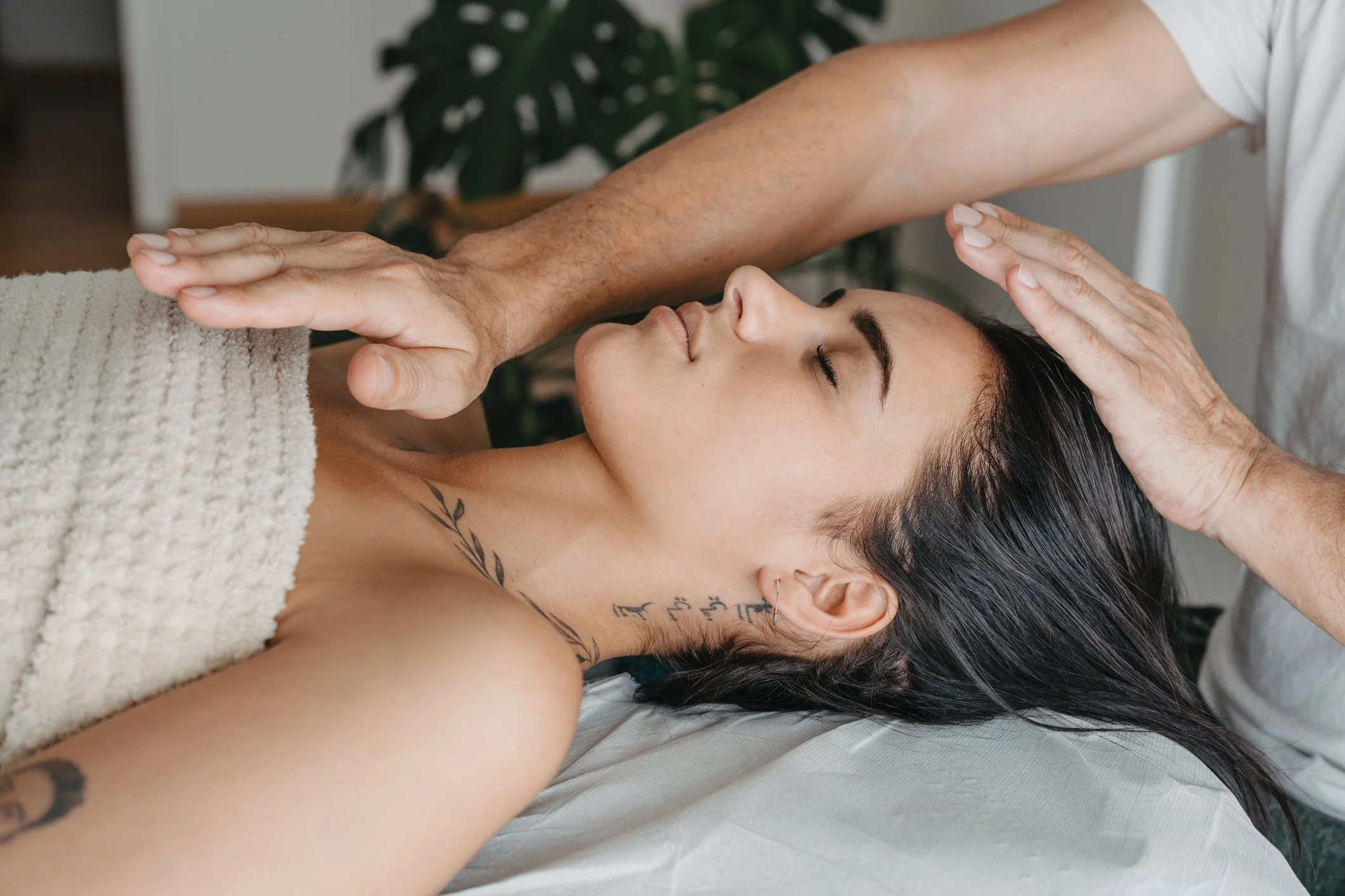 A woman receives a massage while lying on her back with eyes closed, with a therapist applying massage oil to her forehead.