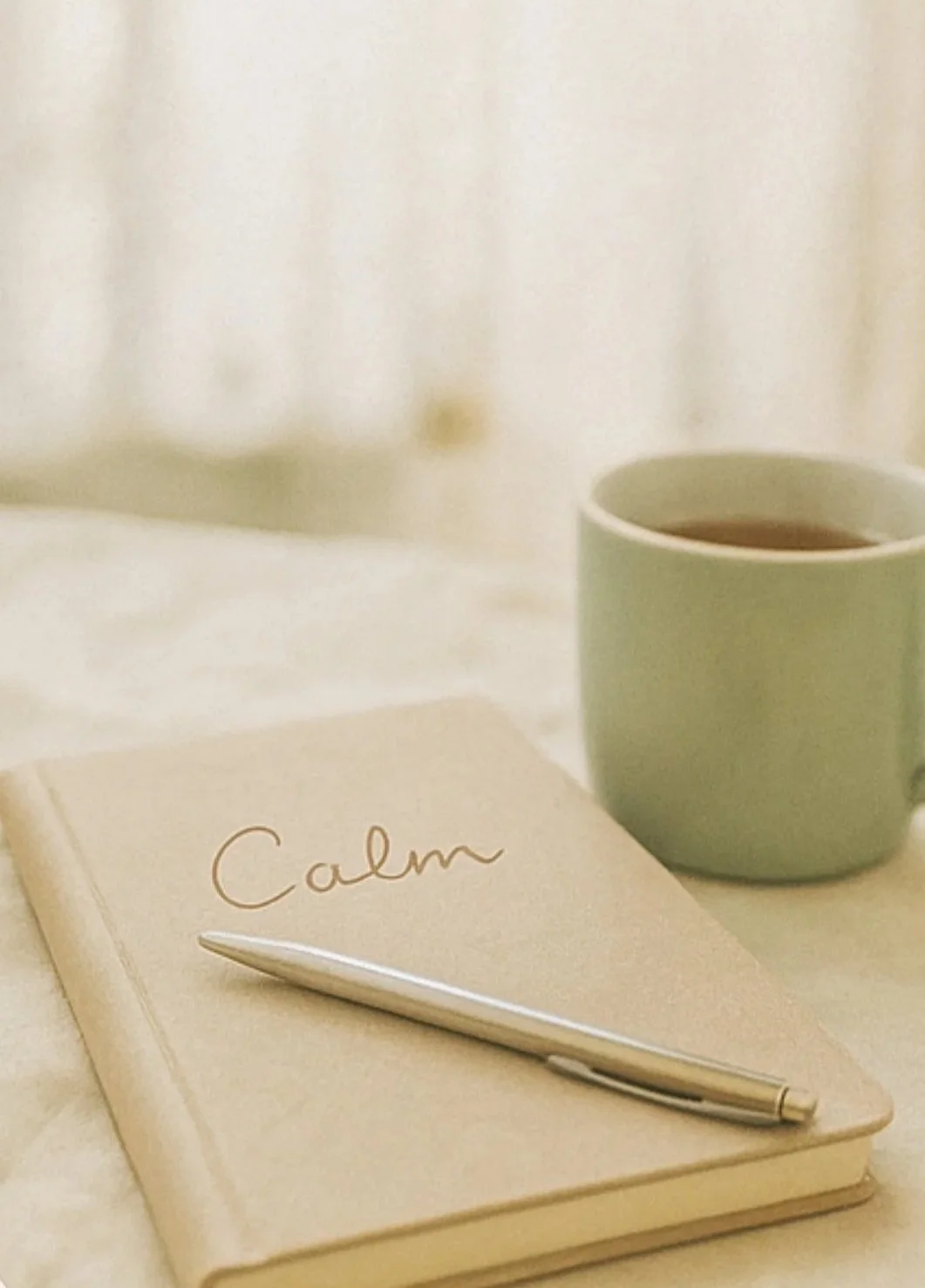 Closed notebook with the word 'Calm' on the cover, a pen, and a mug on a neutral surface.