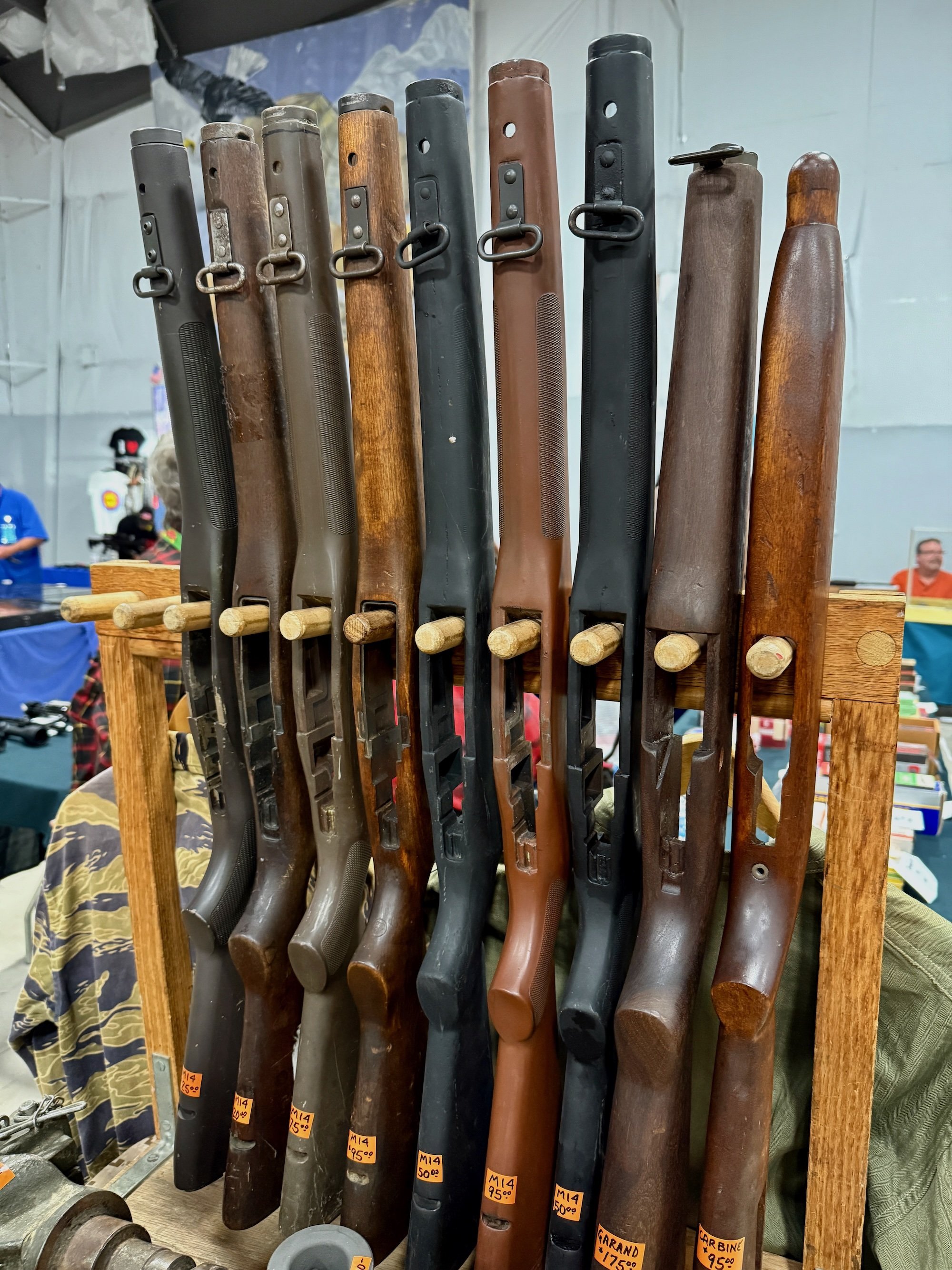 A wooden stand displaying a row of vintage rifles with wooden and metal stocks at a gun show.