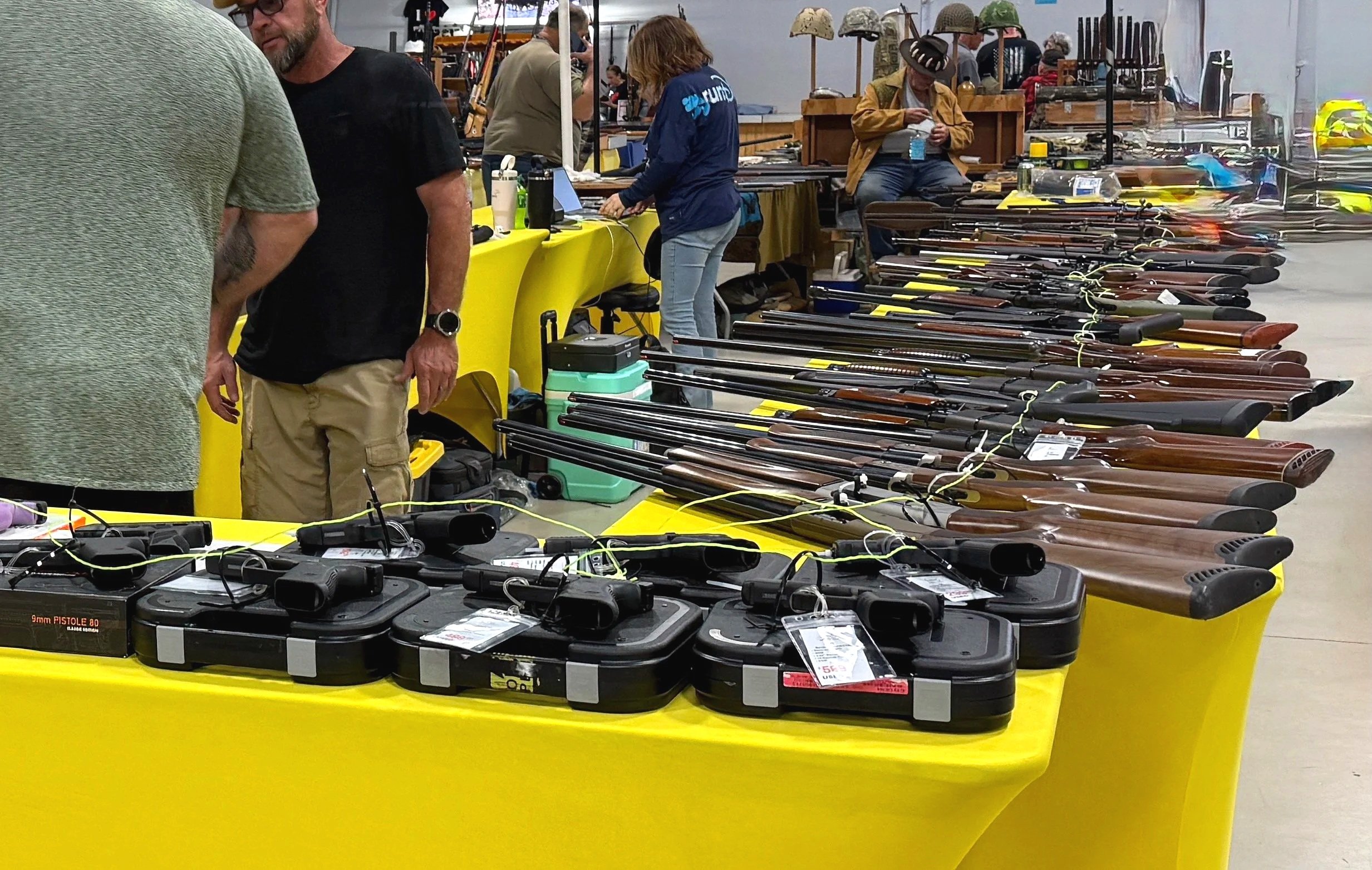 Table with firearms and gun accessories at an indoor marketplace or gun show.