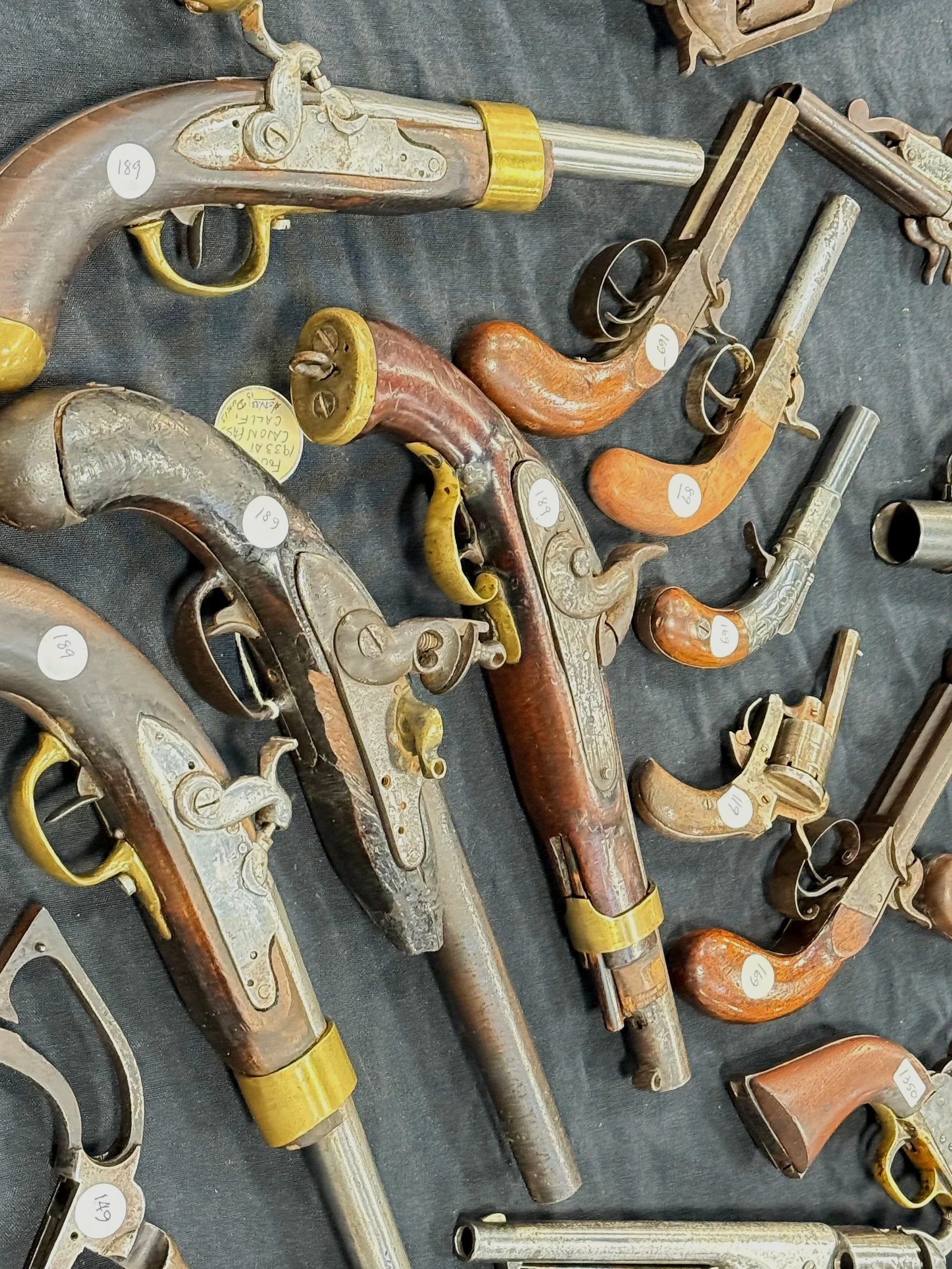 Several antique flintlock pistols with wooden stocks and metal barrels displayed on a black surface, each with a white sticker number.